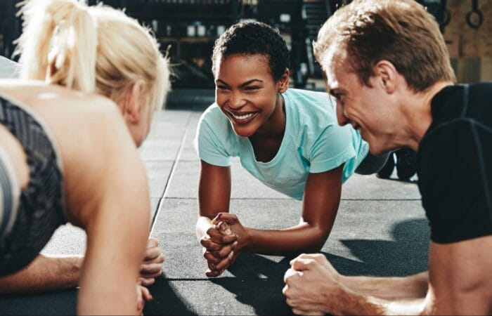 Smiling friends planking together during a gym workout class