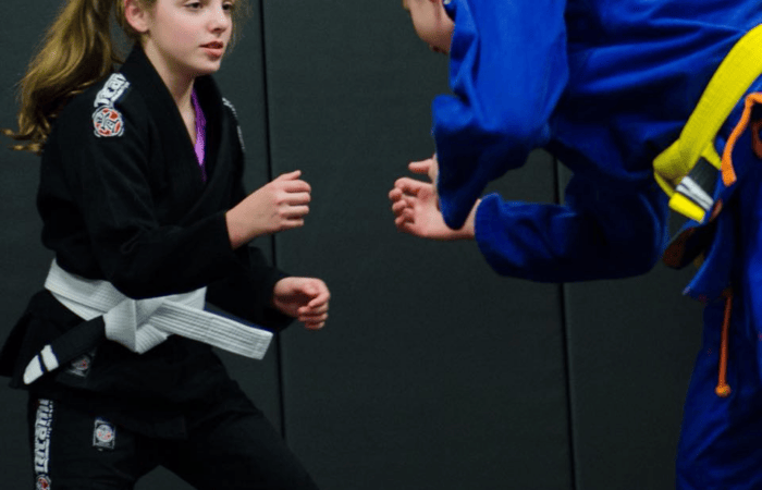 Young girl in a black gi sparring with another student wearing a blue gi