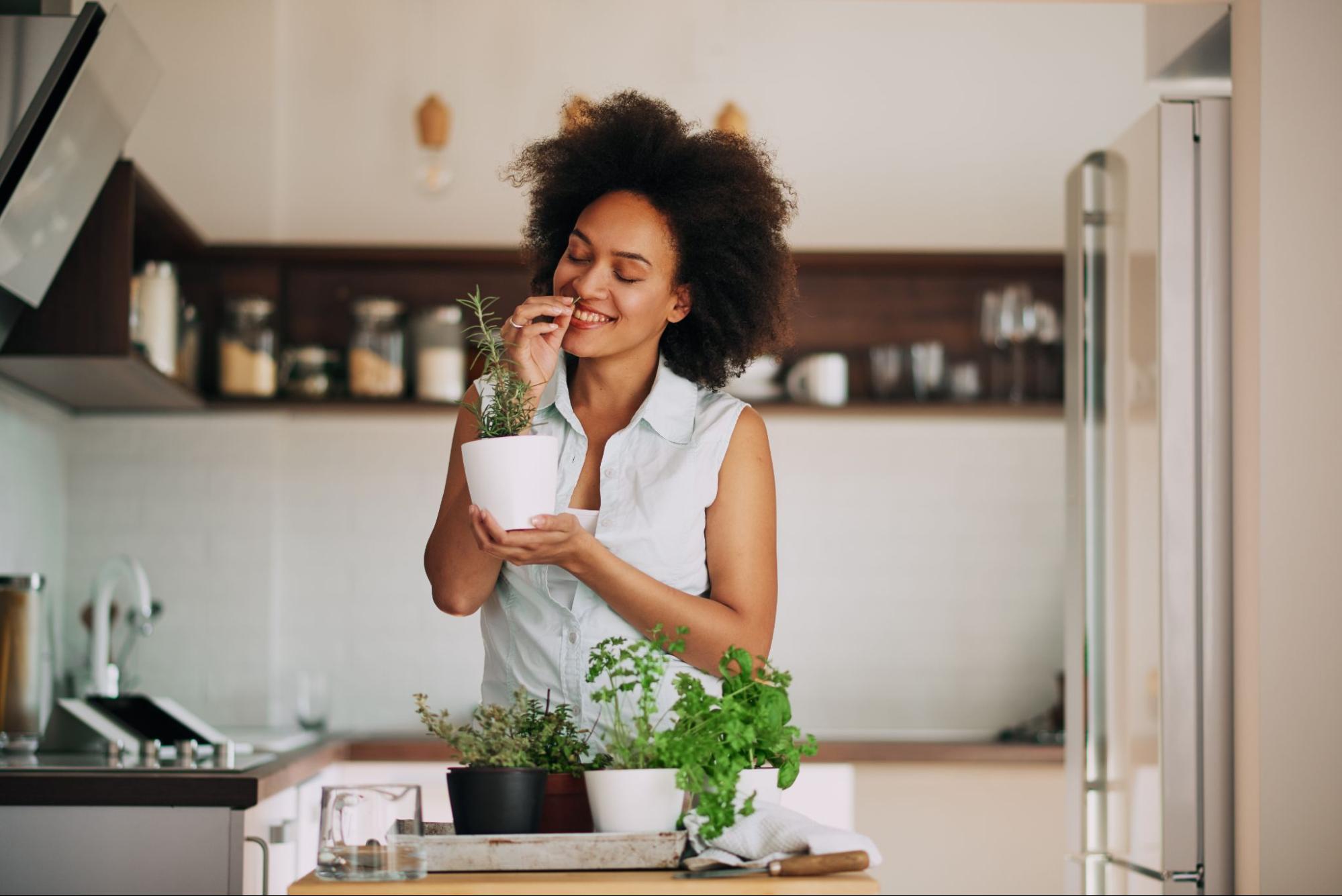 10 Healthy Eating Habits To Try Now 4 Young woman smells fresh herbs she grows in her kitchen to use when flavoring her dishes