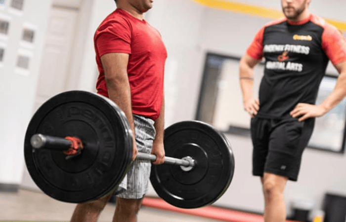 PFMA personal trainer looking on as an athlete lifts a heavy barbell